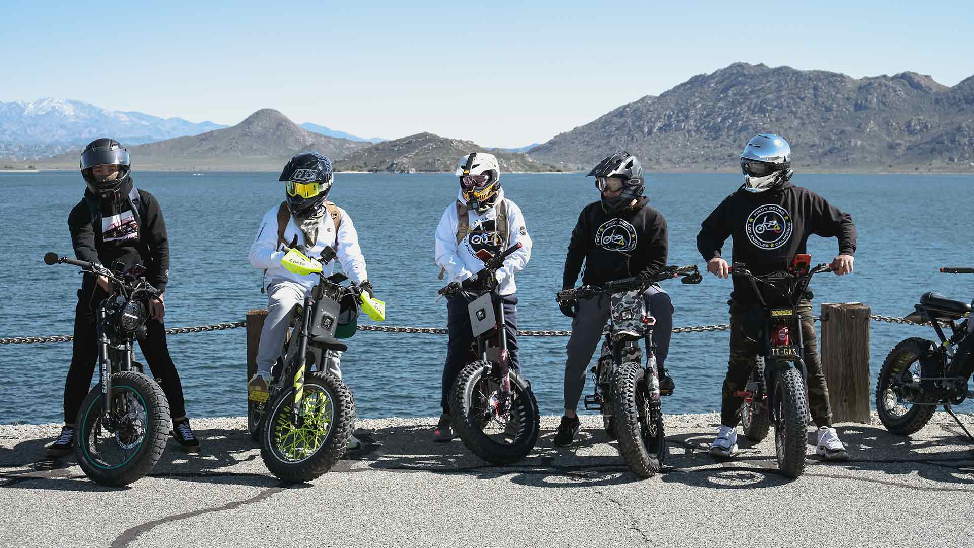 A row of Super73 ebike riders in helmets posing on their bikes in front of a lake
