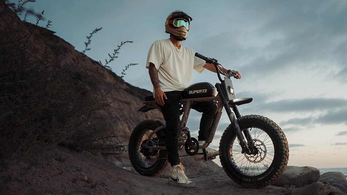 A young man in a helmet sitting on a SUPER73 R Series ebike on a dirt road