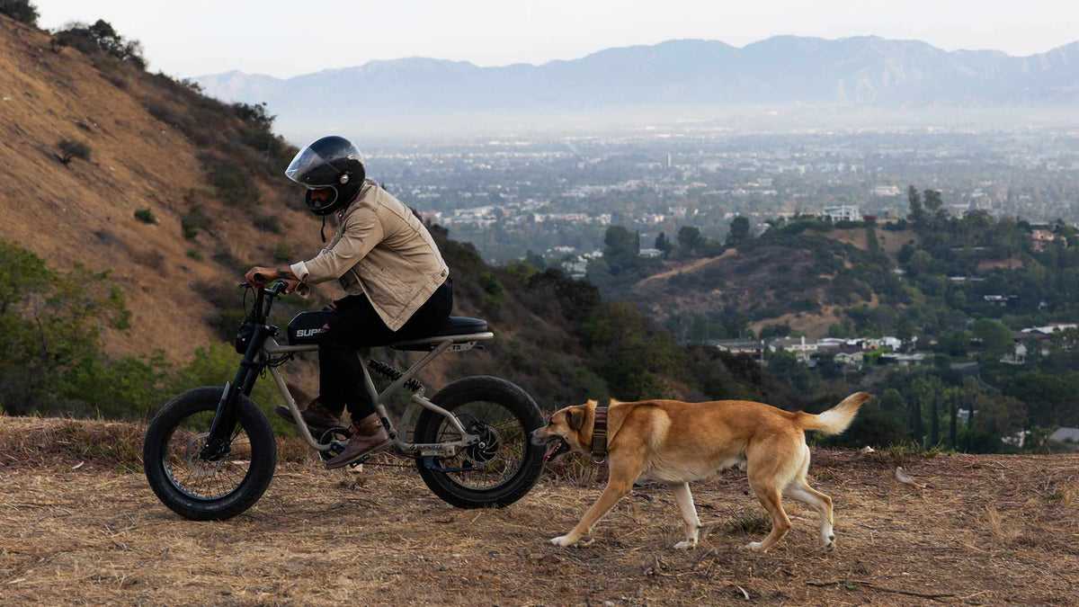 Young man in helmet riding a Super73 ebike on a dirt trail with his dog
