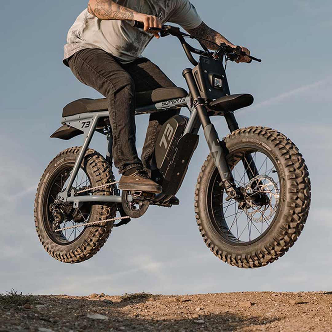 Lifestyle image of a rider doing a jump trick on their S Adventure on a dirt hill and wearing a helmet.